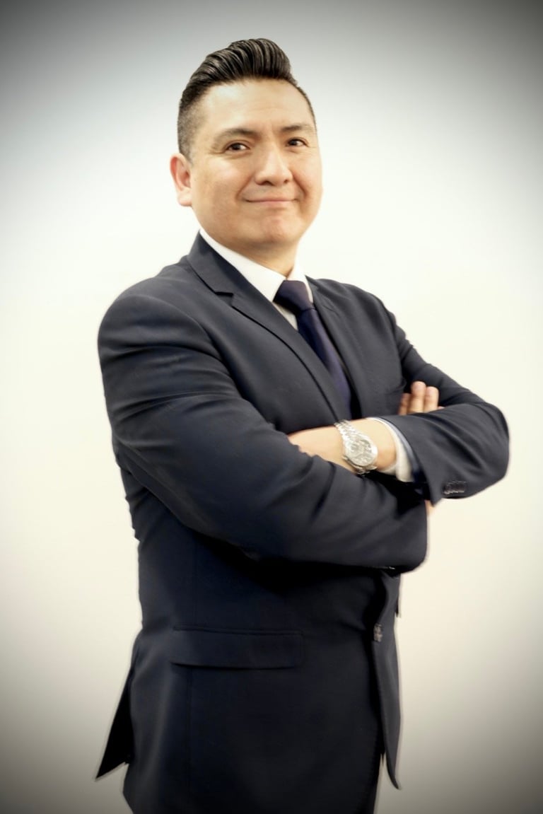 Professional headshot of a man in dark suit and tie with arms crossed, smiling at camera against white background